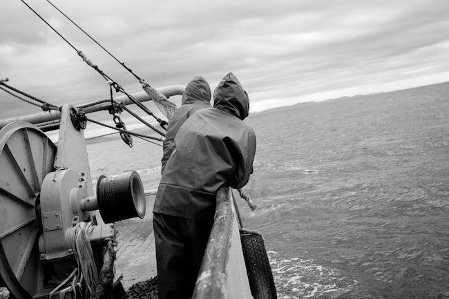 Two crew in oilskins at the rail of a fishing vessel