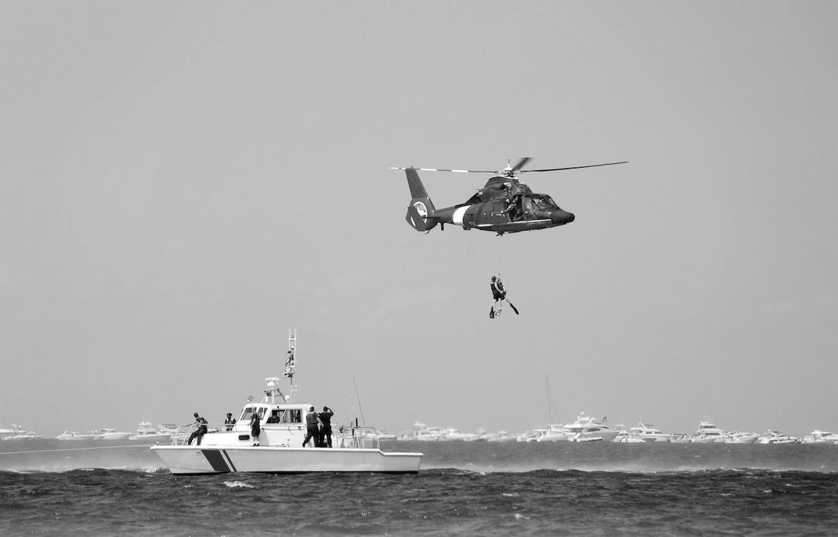 Rescue helicopter winching a person above a patrol boat