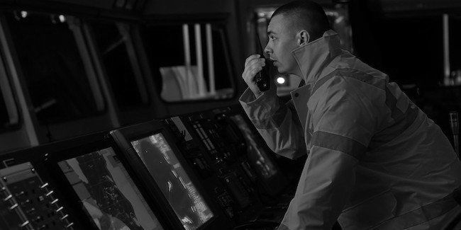 Officer on a ship's bridge using a radio beside navigation screens