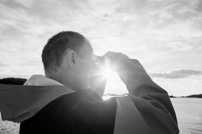 Man scanning the horizon with binoculars against the sun