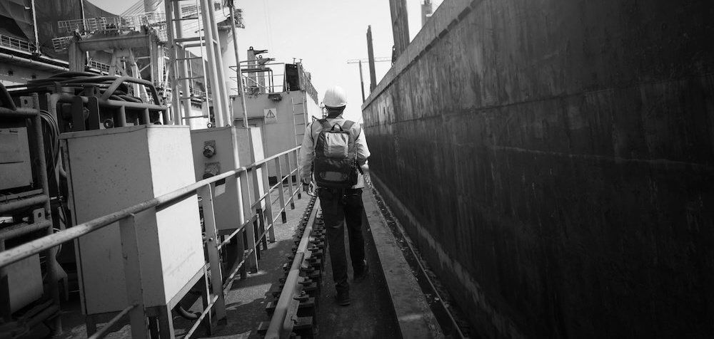 Worker in a hard hat walking along a ship's narrow side deck