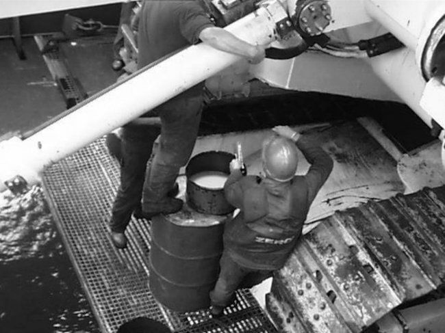 Crew handling a drum on a deck grating, seen from above